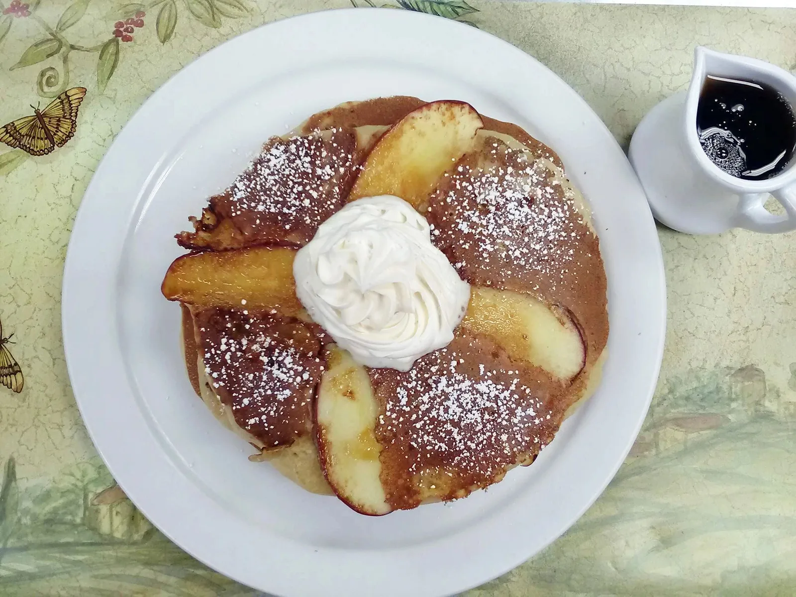 Pancakes with caramelised apples, powdered sugar and whipped cream, with a jug of syrup
